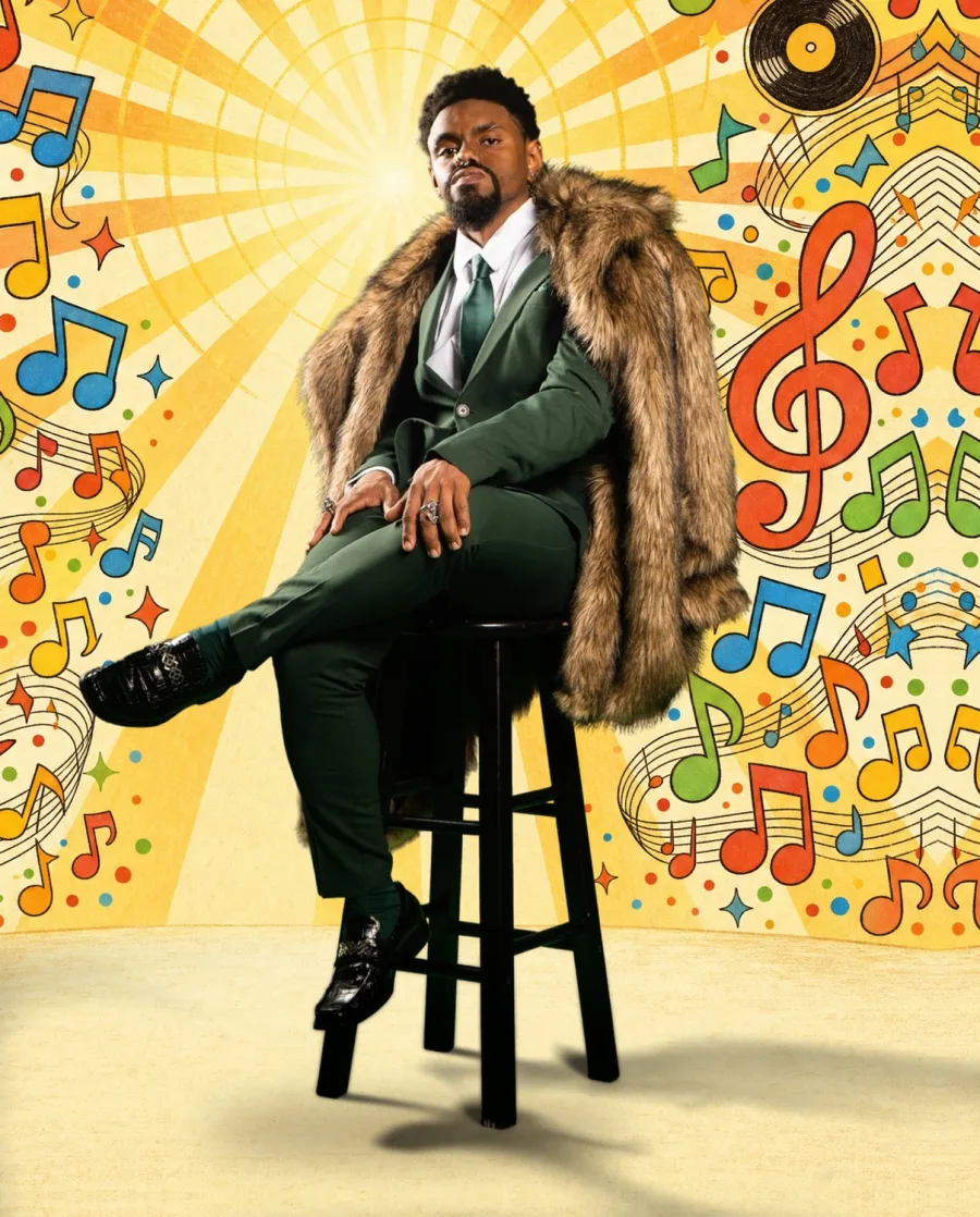 Mal Best in a green suit and fur coat, seated on a stool in front of a colorful musical backdrop